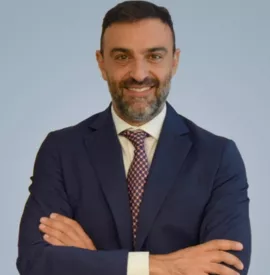 Persona in abito blu con braccia incrociate su sfondo neutro.