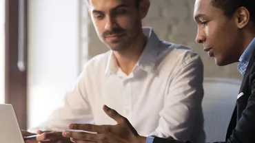 Due persone discutono davanti a un laptop in ufficio.