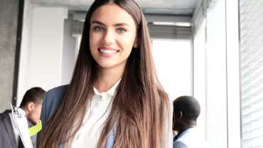 Persona sorridente con capelli lunghi, in un ufficio.
