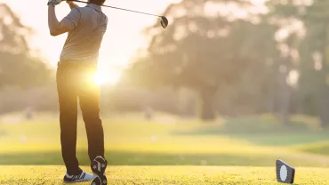 Persona gioca a golf al tramonto su un campo verde.