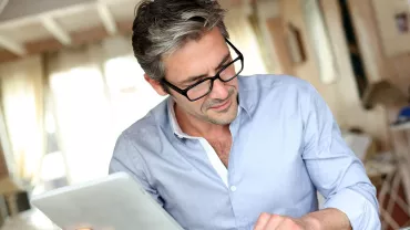 Persona con occhiali che tiene un tablet e scrive su un'agenda.