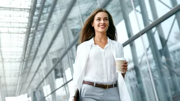 Persona in abbigliamento formale cammina con caffè in mano.