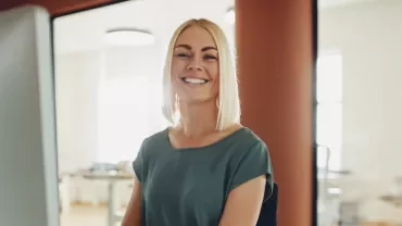 Persona sorridente seduta davanti a un computer in ufficio illuminato.