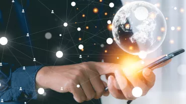 Mano che tiene uno smartphone con elementi digitali e un globo luminoso.