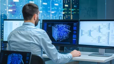 Persona al computer analizza dati su più schermi.