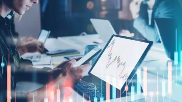 Persone lavorano al computer con grafici finanziari sullo schermo.
