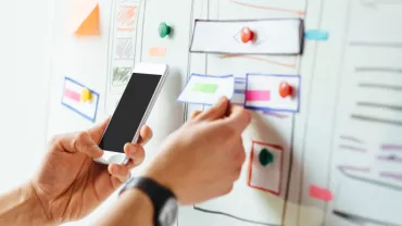 Persona che utilizza uno smartphone e osserva un progetto su lavagna