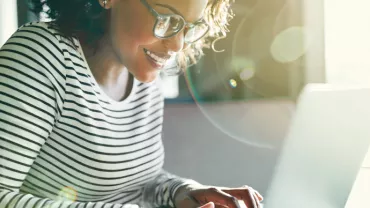 Persona sorridente che utilizza un laptop, con luce solare che entra dalla finestra.
