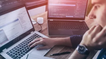 Persona al lavoro su più laptop con codice sullo schermo.