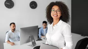 Persona sorridente con occhiali in un ufficio davanti a computer.