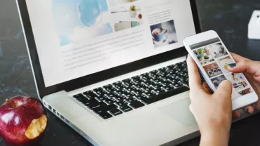 Persona che usa smartphone e laptop, con una mela e una pianta a lato.