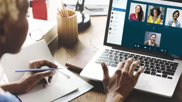 Persona che partecipa a una videochiamata su laptop con appunti.