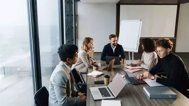 Riunione d'ufficio in corso attorno a un tavolo con laptop.