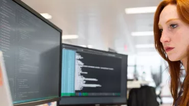 Persona che lavora al computer con codice su due monitor.