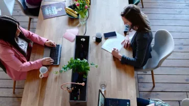 Persone che lavorano a un tavolo con computer portatili e piante.
