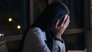 Persona davanti al computer con mani sul viso in un ufficio di notte.