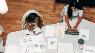 Persone al lavoro in un ufficio con documenti e laptop su un tavolo.