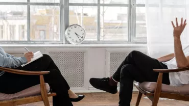 Persona in ufficio parla con professionista seduta di fronte.
