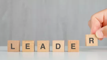 Blocchi di legno con la parola “LEADER” su sfondo grigio.