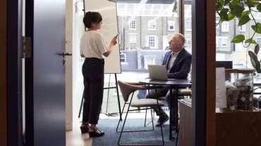 Persona parla davanti a una lavagna in un ufficio con una finestra grande.