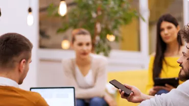 Persone discutono in un ufficio moderno con piante e luci soffuse.