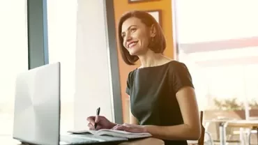 Persona sorridente seduta al tavolo con laptop aperto.