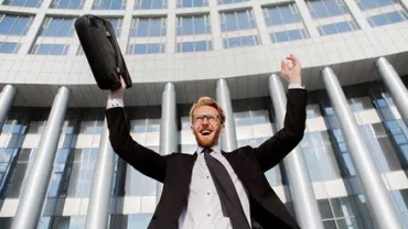 Persona sorridente solleva una valigetta davanti a un edificio moderno.