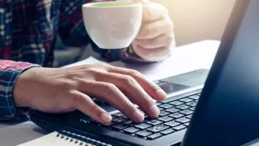 Persona al lavoro su un laptop tenendo una tazza da caffè.