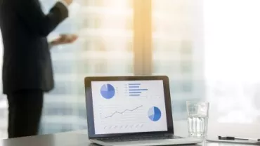 Ufficio moderno con laptop e grafici su schermo.