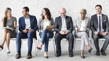 Gruppo di persone sedute in attesa, indossano abiti formali.