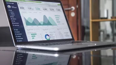 Computer portatile su un tavolo con grafici e dati sullo schermo.