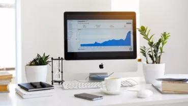 Scrivania con computer e grafico a schermo, piante e tazza di caffè.