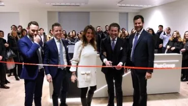 Inaugurazione di un nuovo ufficio con persone sorridenti che tagliano un nastro rosso.