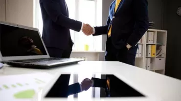 Stretta di mano in ufficio con dispositivi sul tavolo.