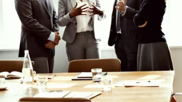 Persone in abiti formali discutono davanti a un tavolo da riunione.