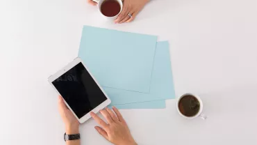 Due persone con tazze di tè e un tablet su un tavolo.