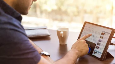 Persona che usa un tablet al tavolo con tazza di caffè.