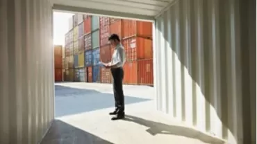 Persona in piedi vicino a container colorati, con documenti in mano.