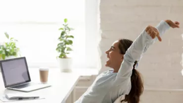 Persona felice si allunga alla scrivania accanto a un laptop.
