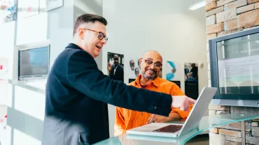 Persona indica uno schermo del laptop a un'altra in ufficio luminoso
