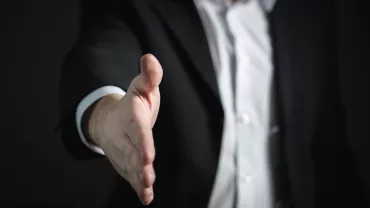Persona in abito formale tende la mano per una stretta.
