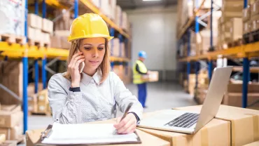Persona con casco giallo al telefono in magazzino.