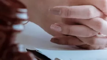 Mani intrecciate su una scrivania con un martelletto e documenti.
