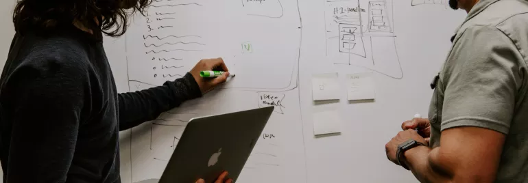Due persone discutono di un piano illustrato su una lavagna.