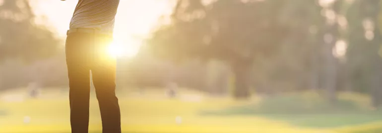 Persona gioca a golf al tramonto su un campo verde.