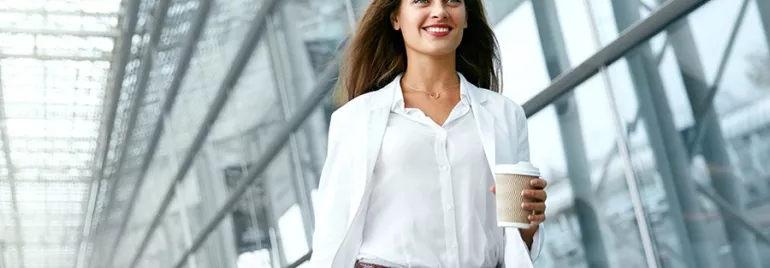 Persona in abbigliamento formale cammina con caffè in mano.
