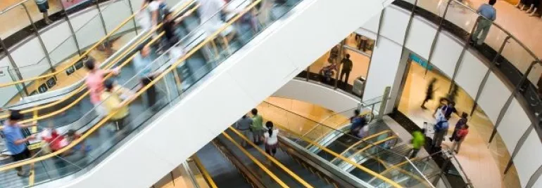 Centro commerciale affollato con scale mobili in movimento.