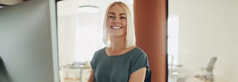 Persona sorridente seduta davanti a un computer in ufficio illuminato.