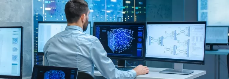 Persona al computer analizza dati su più schermi.