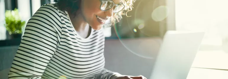 Persona sorridente che utilizza un laptop, con luce solare che entra dalla finestra.